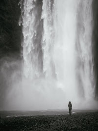 Man standing on shore against storm clouds