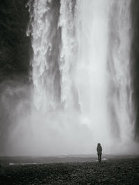 Rear view of person standing against skogafoss waterfall