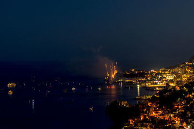 High angle view of illuminated buildings by sea against sky at night