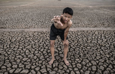 Portrait of shirtless boy standing on cracked land