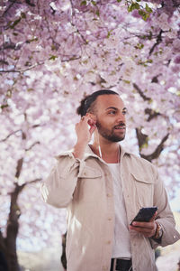 Young man standing under cherry blossom and using phone