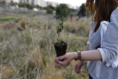 Midsection of woman holding plant while standing on field