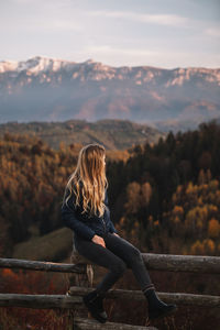 Beautiful blonde woman relaxing on the fence in the autumn mountains at sunset. travel concept.