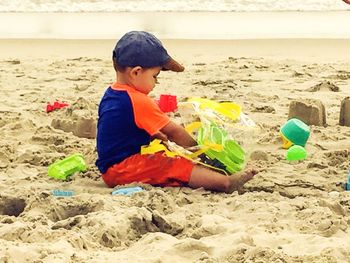 Boy playing in sand at beach against sky