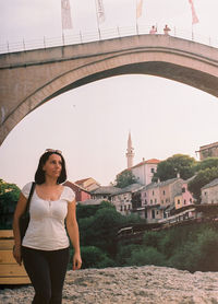 Portrait of woman standing against bridge in city