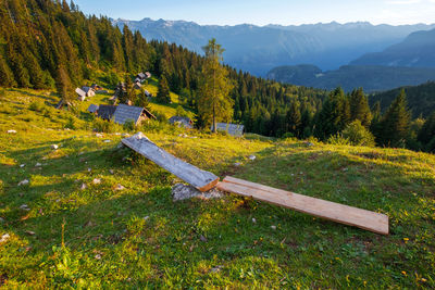Bench on field by trees against mountains