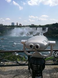 Coin-operated binoculars by river against sky