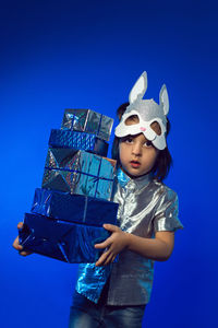 Christmas baby boy in hare mask with gift in studio on blue wall background