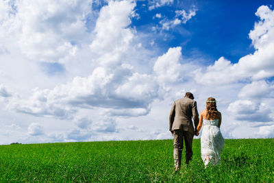 Rear view of newlywed couple walking on land against sky