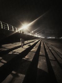 Shadow of man on illuminated railroad tracks against sky