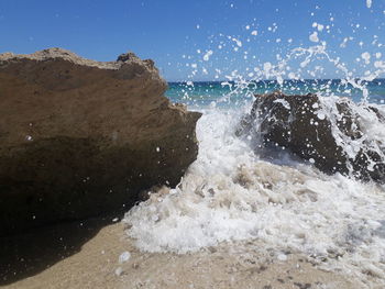 Waves splashing on rocks at shore against sky