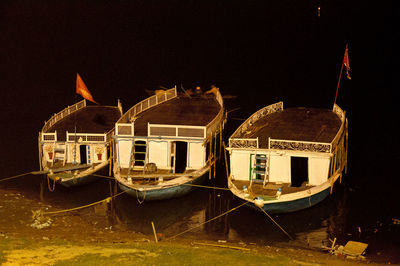 Sailboats moored on sea against illuminated buildings at night