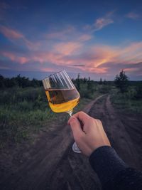 Midsection of person holding drink against sky during sunset