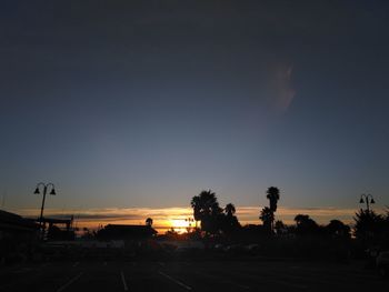 Road by silhouette trees against clear sky during sunset