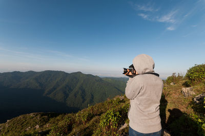Rear view of hiker photographing mountains against sky