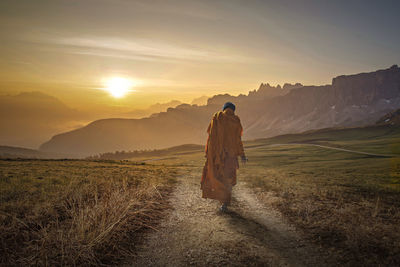 Rear view of man standing on mountain against sky during sunset