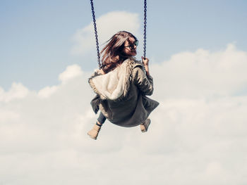 Low angle view of woman on swing against cloudy sky
