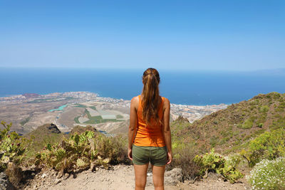 Rear view of woman looking at sea while standing on mountain against sky