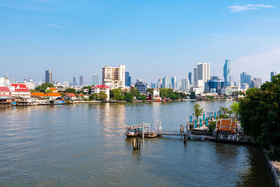 Boats in river by buildings in city against sky