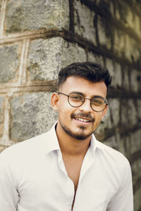 Portrait of smiling young man standing against wall