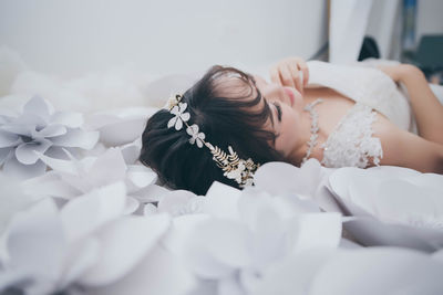 Smiling young bride lying on white paper flowers on bed