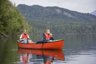 Siblings wearing life jacket canoeing on lake against mountain