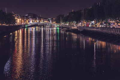 View of calm river in front of illuminated buildings at night