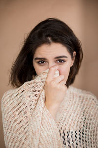 Portrait of young woman covering face against wall