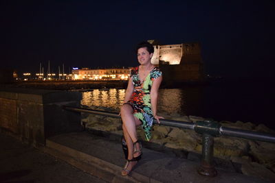 Portrait of young woman sitting on retaining wall at night