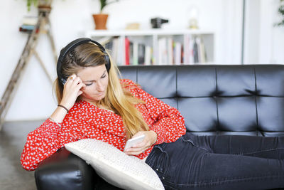 Woman listening to music through headphones on sofa at home