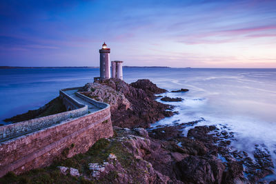 Lighthouse by sea against sky during sunset