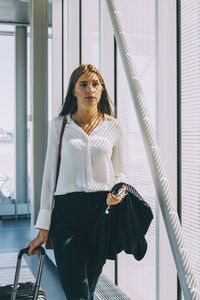 Young businesswoman pulling luggage while walking in corridor at airport