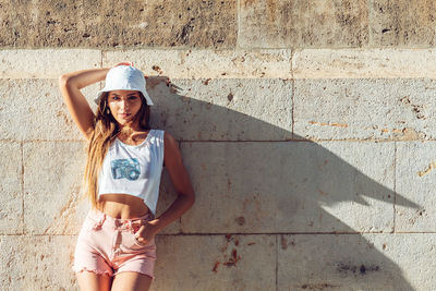 Portrait of young woman standing against wall