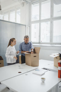 Businessman and businesswoman unpacking cardboard box in new office