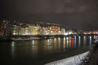 Illuminated buildings by river against sky at night