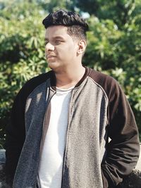 Young man looking away standing against plants