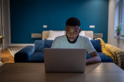 Young focused african american man freelancer working on laptop until late hours at home