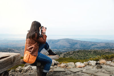 Woman photographing on mountain against clear sky