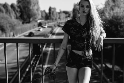 Portrait of young woman standing by railing on footbridge