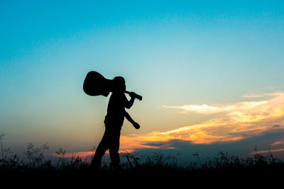 Silhouette man holding guitar against sky during sunset