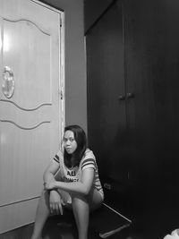 Young woman looking down while sitting on wall at home