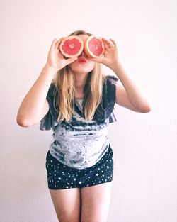 Woman covering eyes with blood orange while standing against white background