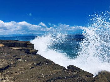 Sea waves splashing on rocks against blue sky