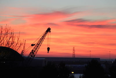 Silhouette cranes at construction site against orange sky