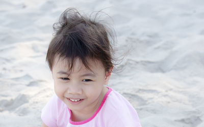 Positive 4 years old baby asian girl, little child smiling and looking to the right on white sand.
