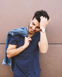 Smiling handsome young man with hand in hair standing against wall