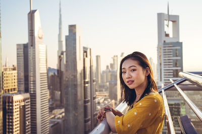Portrait of woman with mobile phone and buildings in city