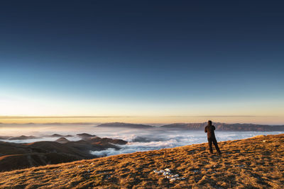 Woman standing on land against sky during sunset