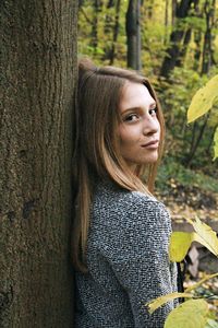 Portrait of woman against tree trunk in forest