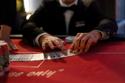 Close-up of a card dealer's hands expertly dealing cards on a vibrant red casino table.